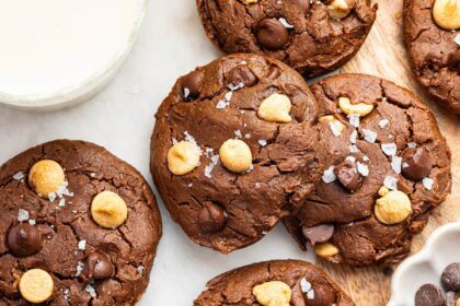 9 chocolate peanut butter cookies spread out on a counter. All of the cookies are topped with flaky sea salt.