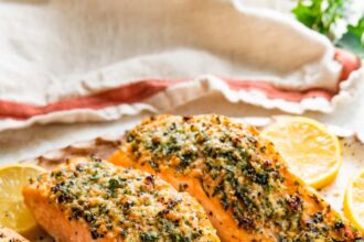 Four parmesan crusted salmon filets served on a speckled tray with multiple lemon slices.