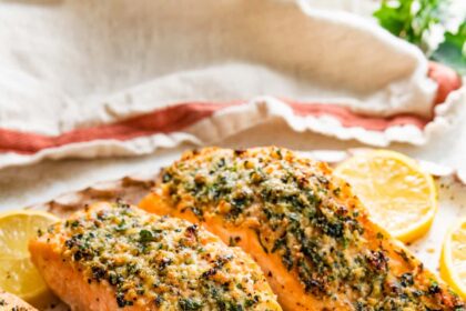 Four parmesan crusted salmon filets served on a speckled tray with multiple lemon slices.