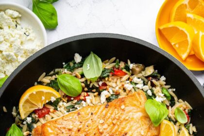 Two salmon filets in a skillet served over a bed of orzo combined with roasted red peppers, chopped dates, feta and swiss chard. It