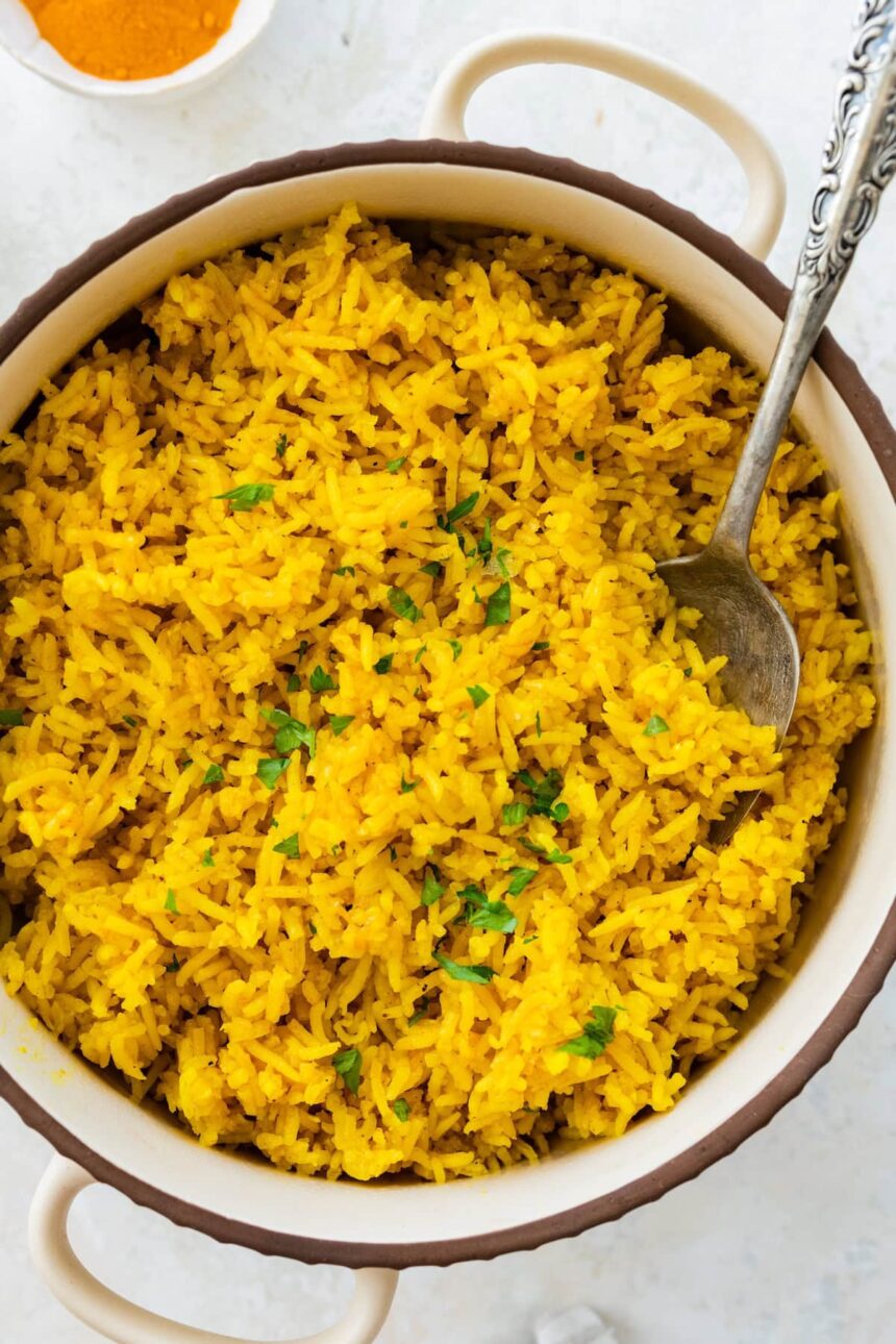 A pot of cooked turmeric rice topped with fresh parsley. There is a silver spoon in the rice.